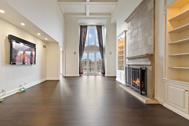 unfurnished living room with a large fireplace, built in features, baseboards, dark wood-style flooring, and beam ceiling