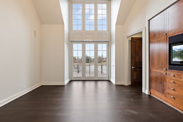 interior space with vaulted ceiling, dark wood-type flooring, and baseboards