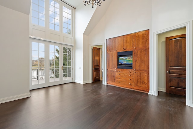 unfurnished living room featuring high vaulted ceiling, dark wood-style flooring, baseboards, and an inviting chandelier