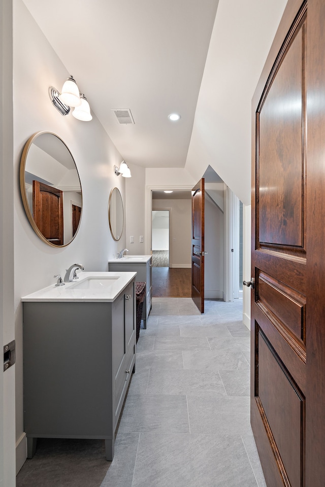 bathroom with baseboards, visible vents, two vanities, and a sink