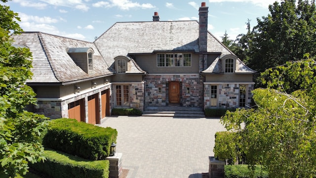 french provincial home featuring a garage, stone siding, a high end roof, and decorative driveway