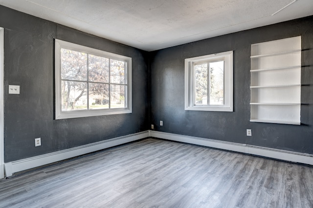 spare room with built in shelves, light wood-type flooring, and a textured ceiling