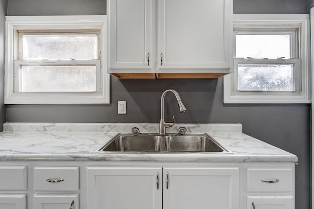 kitchen with white cabinets, light stone counters, and sink