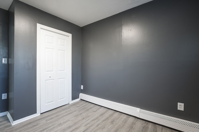 unfurnished bedroom with a closet, light hardwood / wood-style floors, and a baseboard heating unit