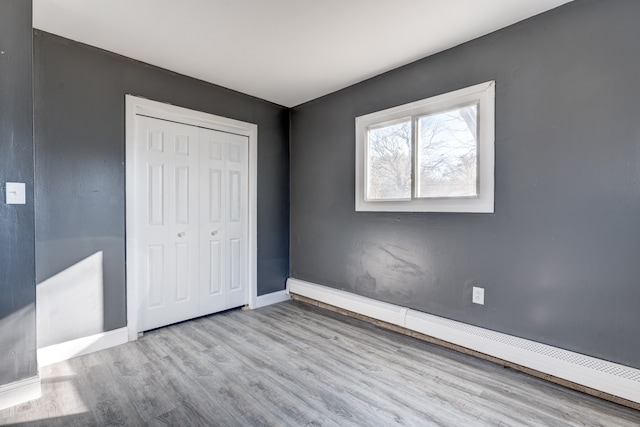 unfurnished bedroom with a closet, baseboard heating, and light hardwood / wood-style flooring