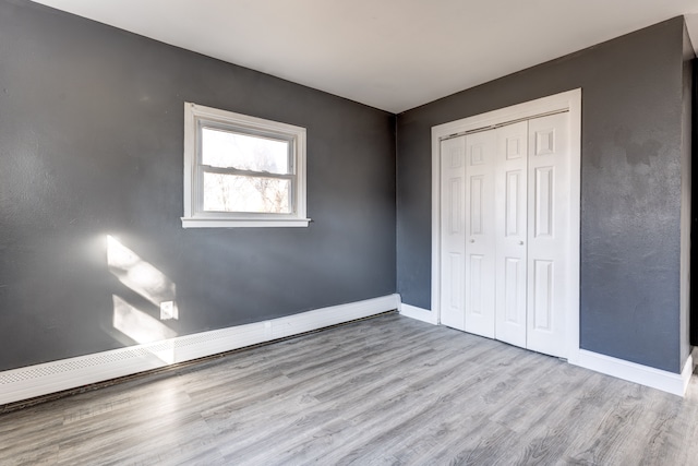 unfurnished bedroom featuring light hardwood / wood-style floors, baseboard heating, and a closet