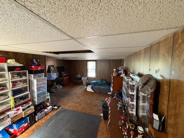 unfurnished bedroom featuring dark colored carpet, a drop ceiling, and wooden walls