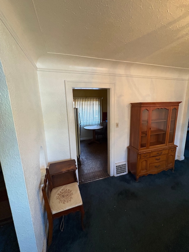 interior space featuring dark colored carpet, a textured ceiling, and ornamental molding