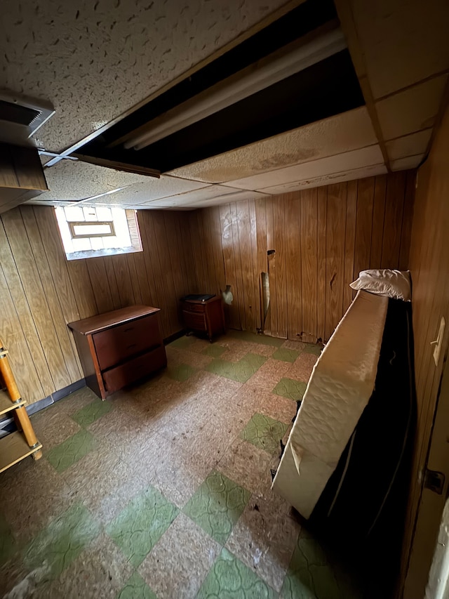 basement with a drop ceiling and wood walls