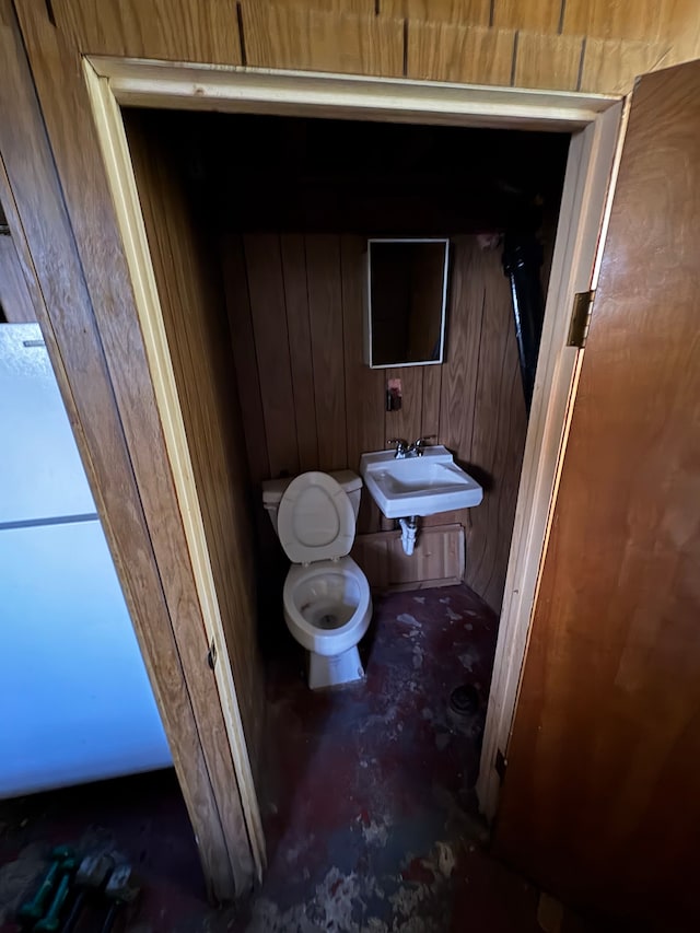 bathroom with wood walls, sink, concrete floors, and toilet