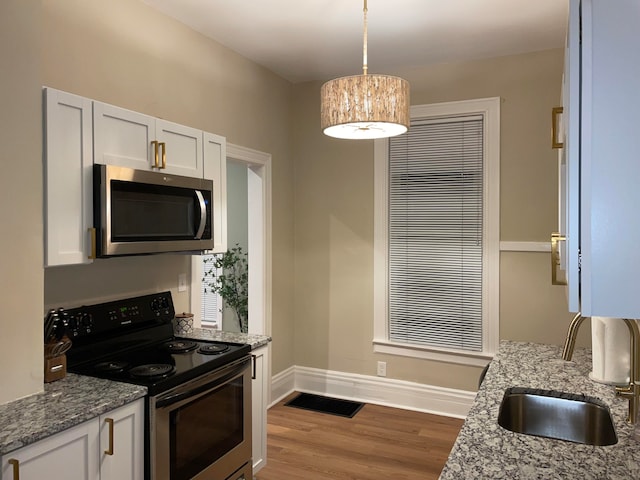 kitchen with stainless steel appliances, sink, light hardwood / wood-style floors, white cabinetry, and hanging light fixtures