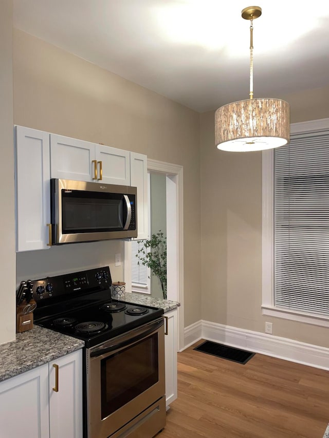 kitchen with stainless steel appliances, light stone counters, pendant lighting, light hardwood / wood-style floors, and white cabinets