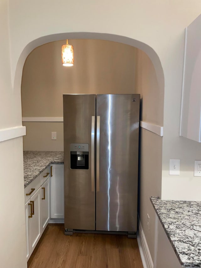 kitchen with light stone countertops, white cabinetry, stainless steel refrigerator with ice dispenser, light hardwood / wood-style floors, and decorative light fixtures