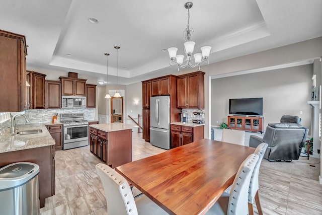 kitchen with a raised ceiling, a kitchen island, decorative light fixtures, and appliances with stainless steel finishes