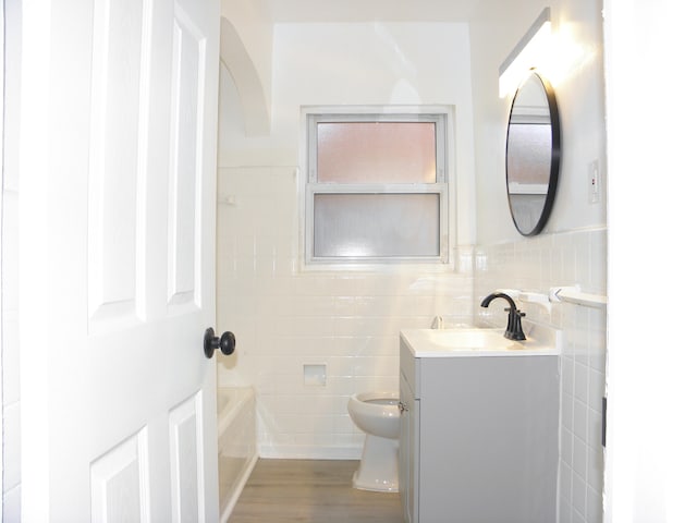 bathroom featuring vanity, a bath, toilet, tile walls, and wood-type flooring