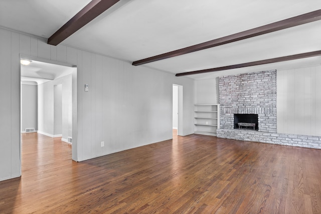 unfurnished living room featuring beam ceiling, wooden walls, a brick fireplace, and dark wood-type flooring