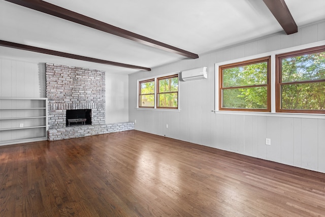 unfurnished living room with hardwood / wood-style flooring, beam ceiling, a fireplace, and a wall unit AC