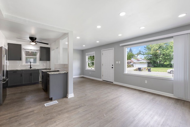 kitchen with decorative backsplash, light stone countertops, ceiling fan, sink, and wood-type flooring