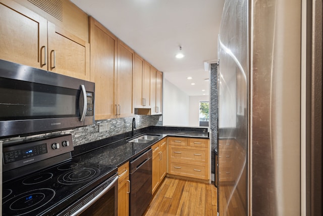 kitchen with dark stone counters, sink, light wood-type flooring, tasteful backsplash, and stainless steel appliances