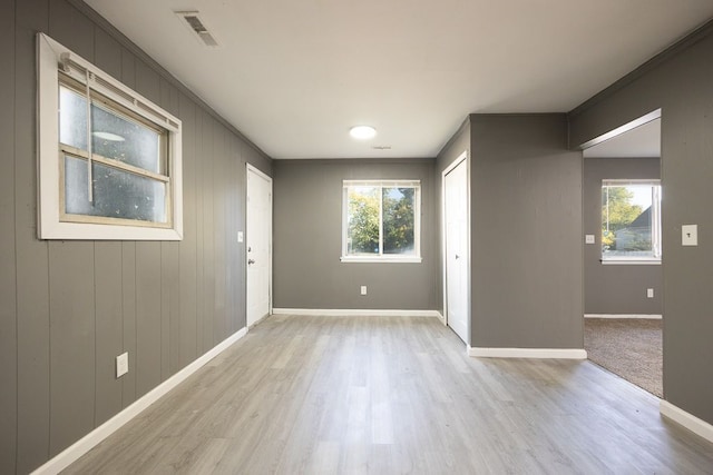 empty room featuring light hardwood / wood-style floors, ornamental molding, and wood walls