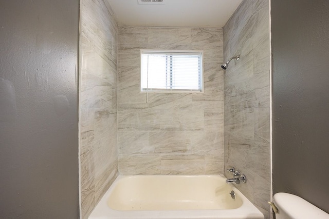 bathroom with tiled shower / bath combo and toilet