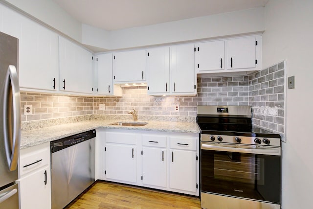kitchen featuring light stone counters, a sink, light wood finished floors, white cabinets, and appliances with stainless steel finishes