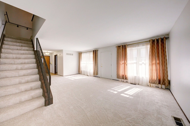 unfurnished living room with light carpet, visible vents, and stairs