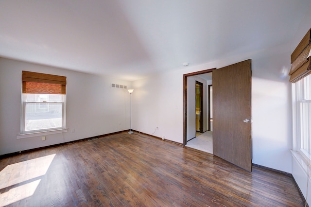 empty room with a wealth of natural light, wood finished floors, and visible vents