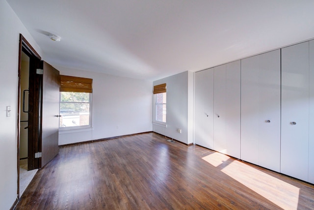 unfurnished bedroom with a closet, baseboards, and dark wood-style flooring