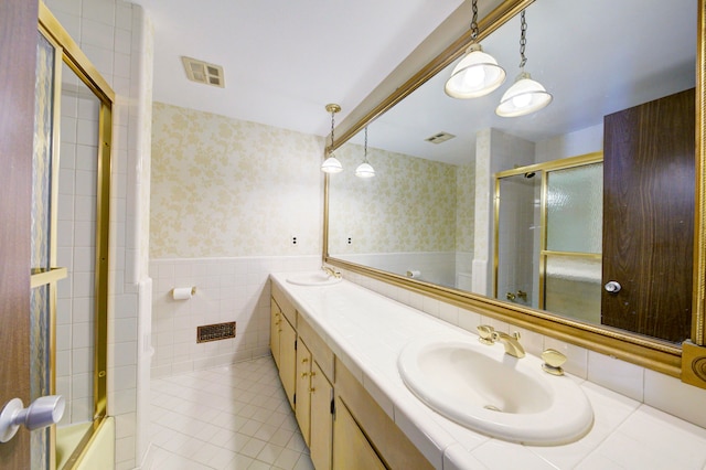 bathroom with tile patterned flooring, vanity, tile walls, and combined bath / shower with glass door