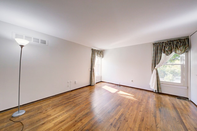 spare room with baseboards, wood finished floors, and visible vents