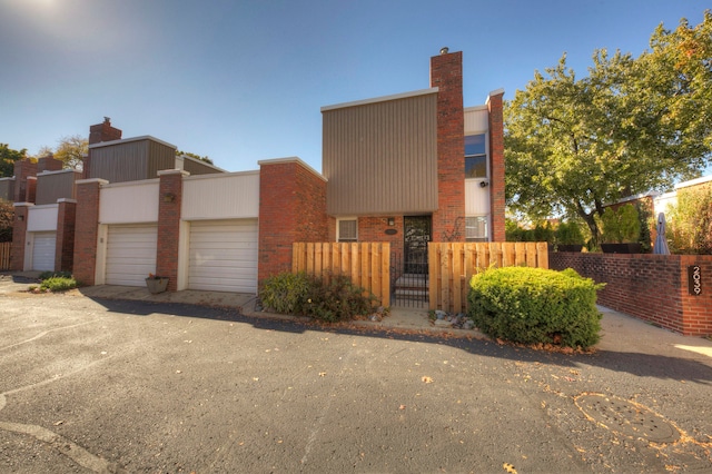 modern home featuring a gate, a chimney, fence private yard, a garage, and brick siding