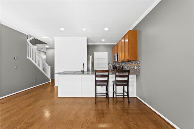 kitchen with stainless steel appliances, dark hardwood / wood-style floors, kitchen peninsula, decorative backsplash, and ornamental molding