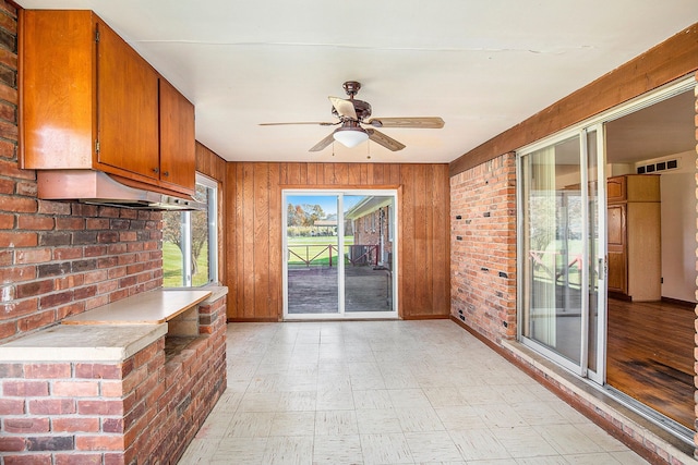 unfurnished living room featuring ceiling fan, brick wall, and wooden walls