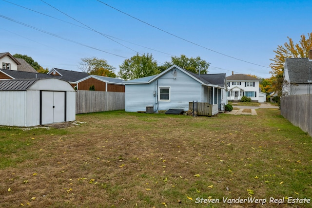 rear view of property featuring a yard, central AC unit, and a storage unit