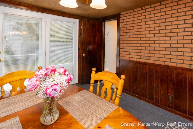 dining space featuring brick wall, a textured ceiling, and wood walls