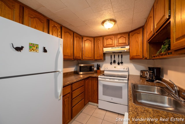 kitchen with sink, light tile patterned floors, dark stone counters, and white appliances