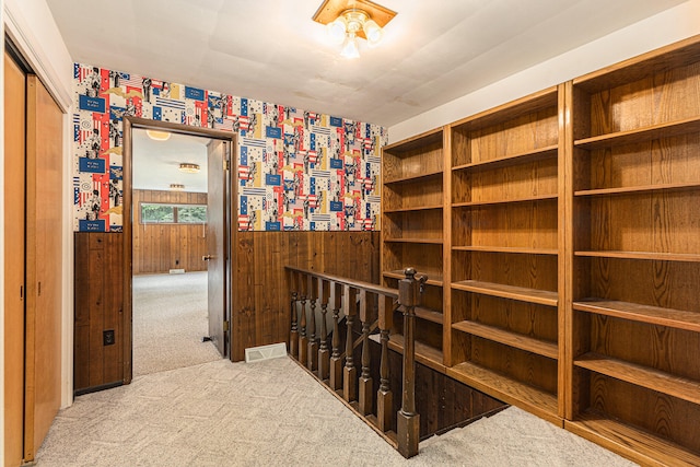 hall featuring light colored carpet and wooden walls