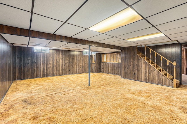 basement with a paneled ceiling, carpet floors, and wooden walls