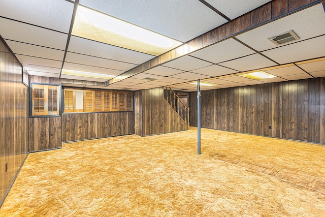 basement with a paneled ceiling, wood walls, and carpet floors