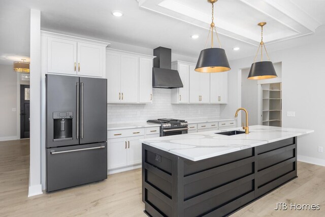 kitchen featuring premium appliances, wall chimney exhaust hood, light wood-style floors, white cabinetry, and a sink