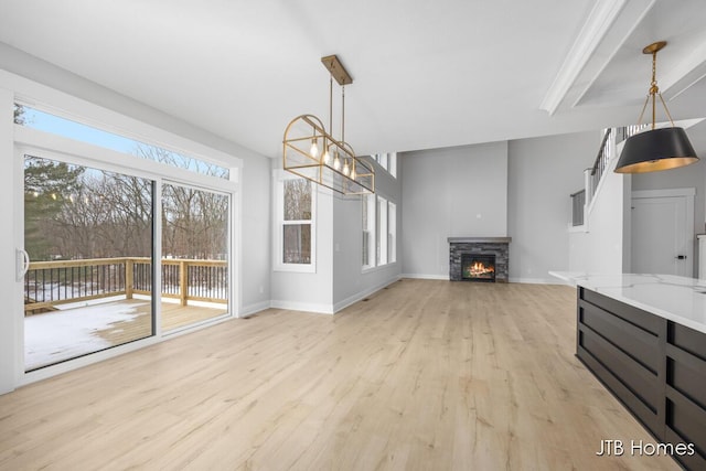 unfurnished living room with a chandelier, a fireplace, light wood-style flooring, and baseboards