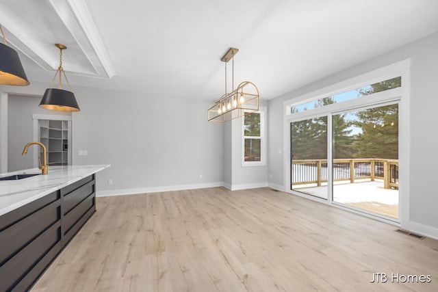 unfurnished dining area with light wood-style floors, visible vents, a sink, and baseboards