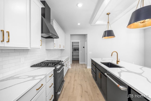 kitchen featuring gas stove, white cabinetry, a sink, wall chimney range hood, and dishwasher