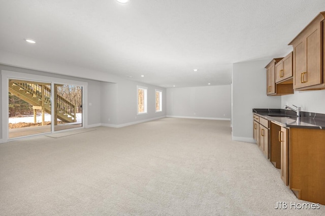 kitchen with light carpet, a sink, baseboards, brown cabinets, and dark countertops