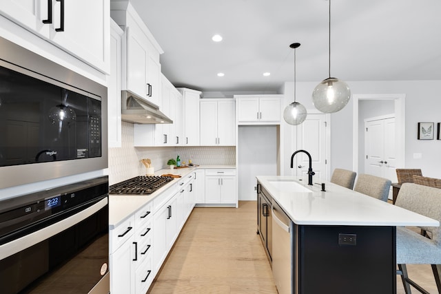 kitchen with sink, stainless steel appliances, backsplash, an island with sink, and white cabinets