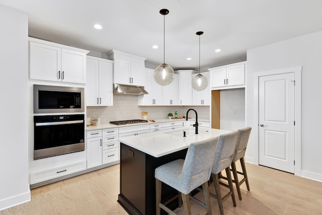 kitchen featuring appliances with stainless steel finishes, a kitchen island with sink, sink, pendant lighting, and light hardwood / wood-style flooring