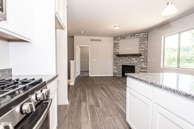 kitchen with white cabinets, decorative light fixtures, a stone fireplace, and light stone countertops