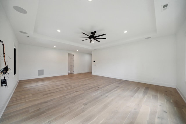 spare room featuring ceiling fan, light wood-type flooring, and a tray ceiling