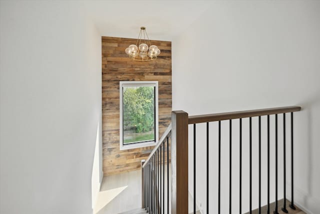 staircase with wood walls and an inviting chandelier